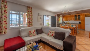 A living room with a sofa, a red ottoman, and a dining area with a table and chairs.