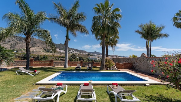 A swimming pool with lounge chairs, palm trees, and a mountainous backdrop.