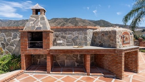 An outdoor kitchen with a stone chimney, a brick oven, and a stone wall backdrop.