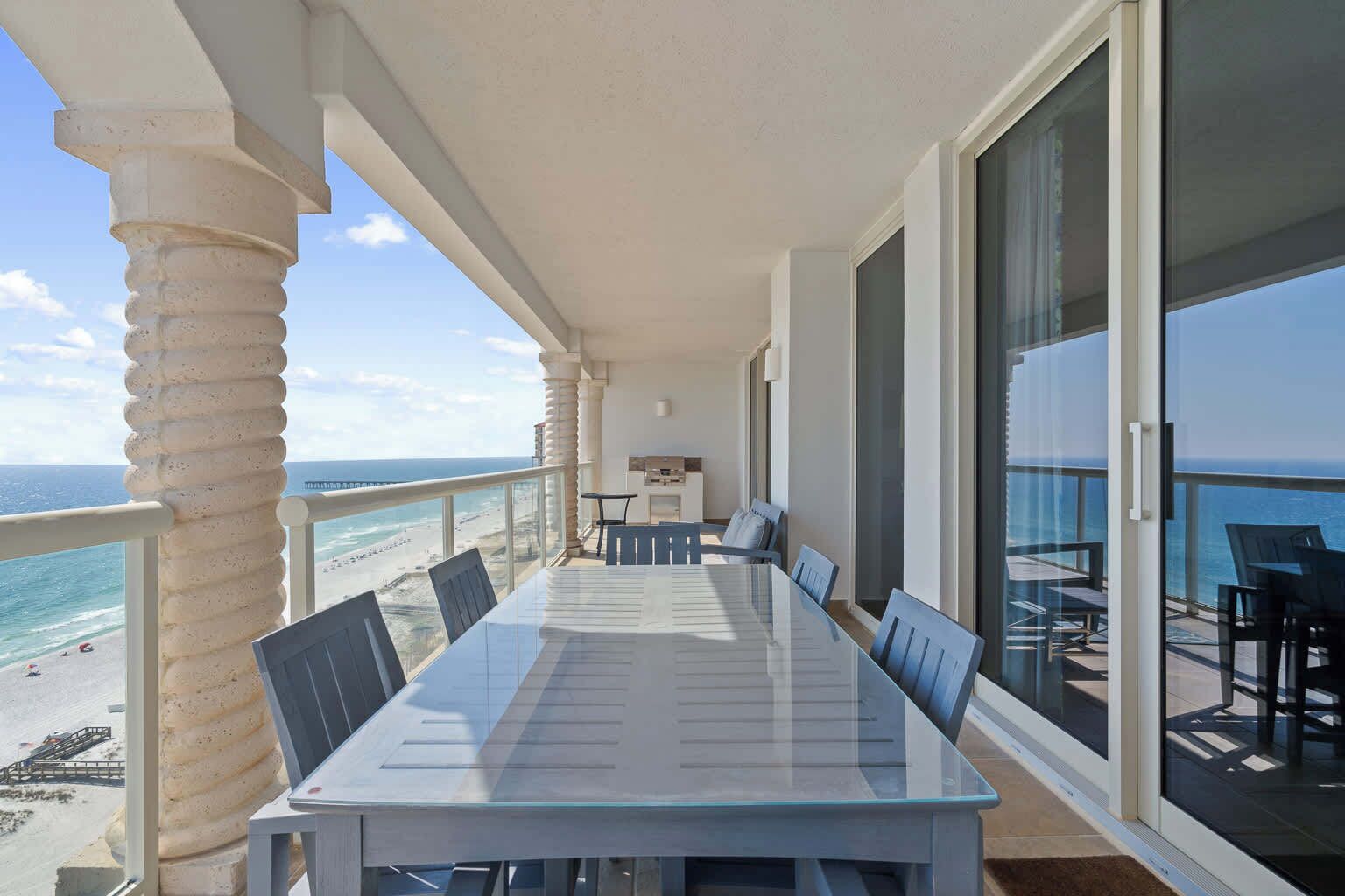 A balcony with a glass table and chairs, overlooking a beach.