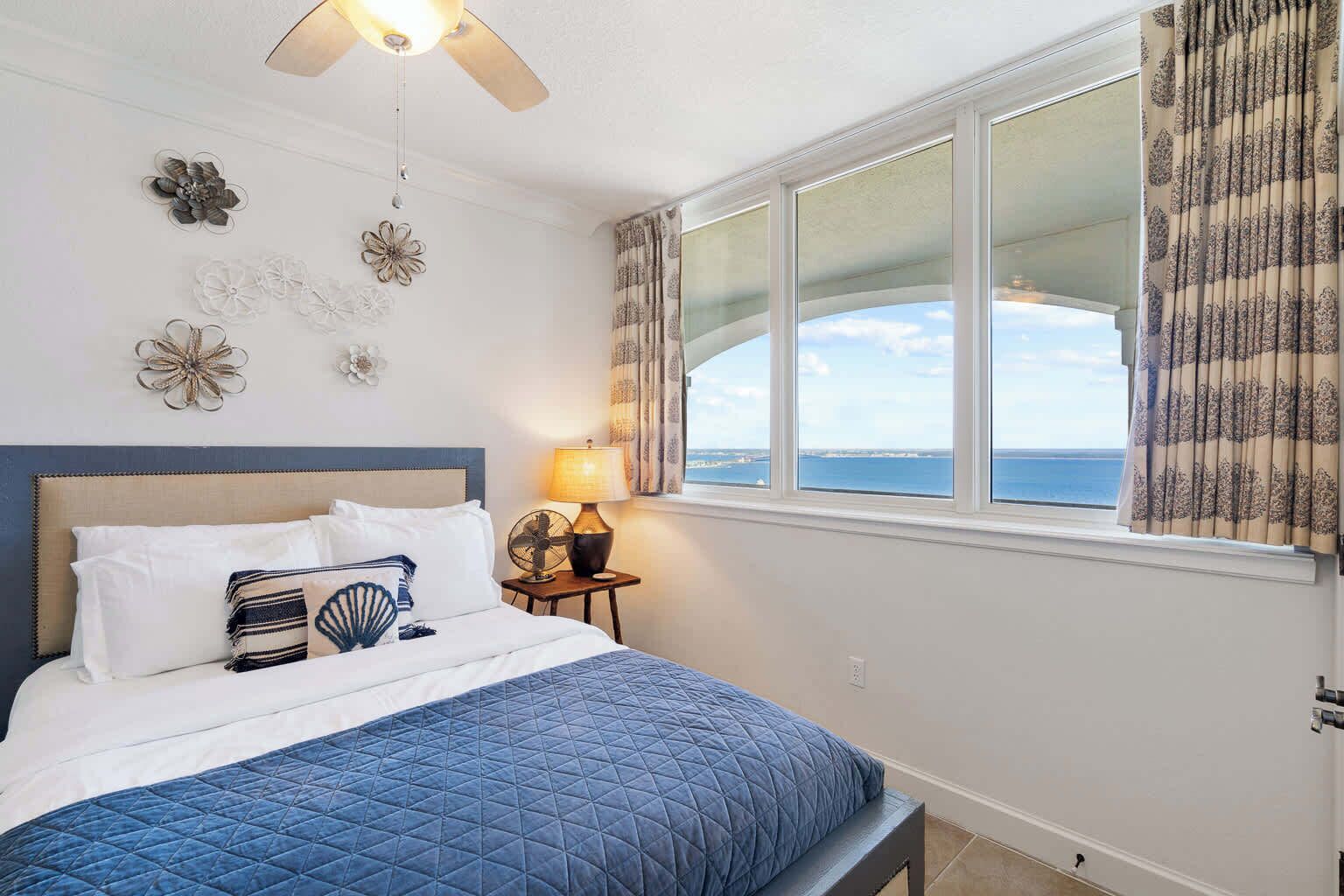 A bedroom with a bed, a ceiling fan, a window with curtains, and wall decor.