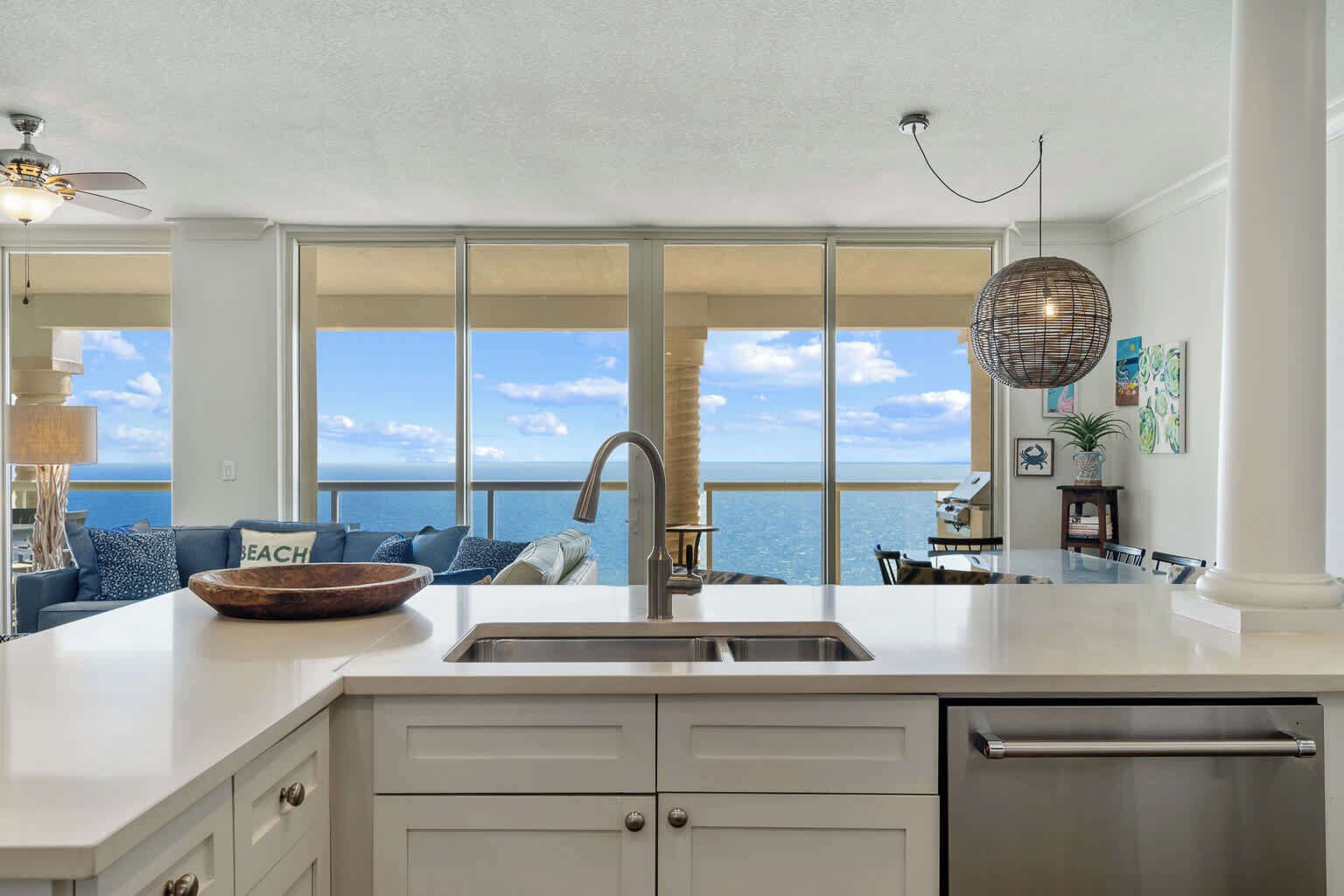A modern kitchen with a large island, a stainless steel sink, and a view of the ocean.