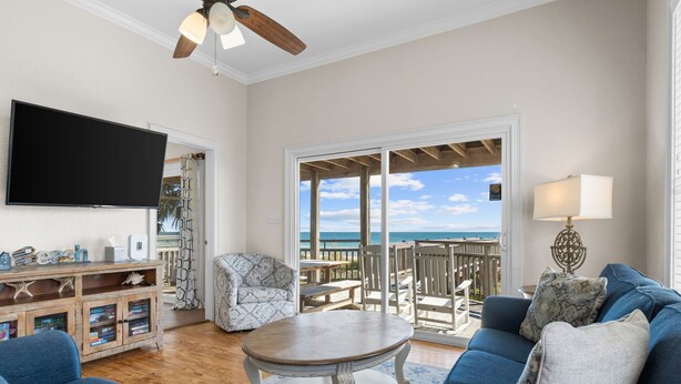 A living room with a TV, a wooden coffee table, blue sofas, and a view of the ocean. - Sunflower Mama, a gulf front home. (St. George Island)
