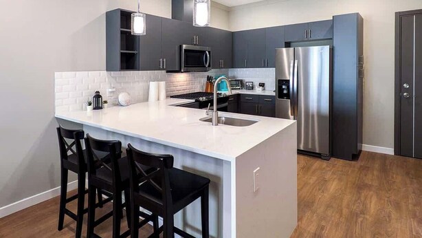 A modern kitchen with a central island, stainless steel appliances, and black bar stools. - 329 Modern 1BR Apt Walk to NJT (Dunellen)