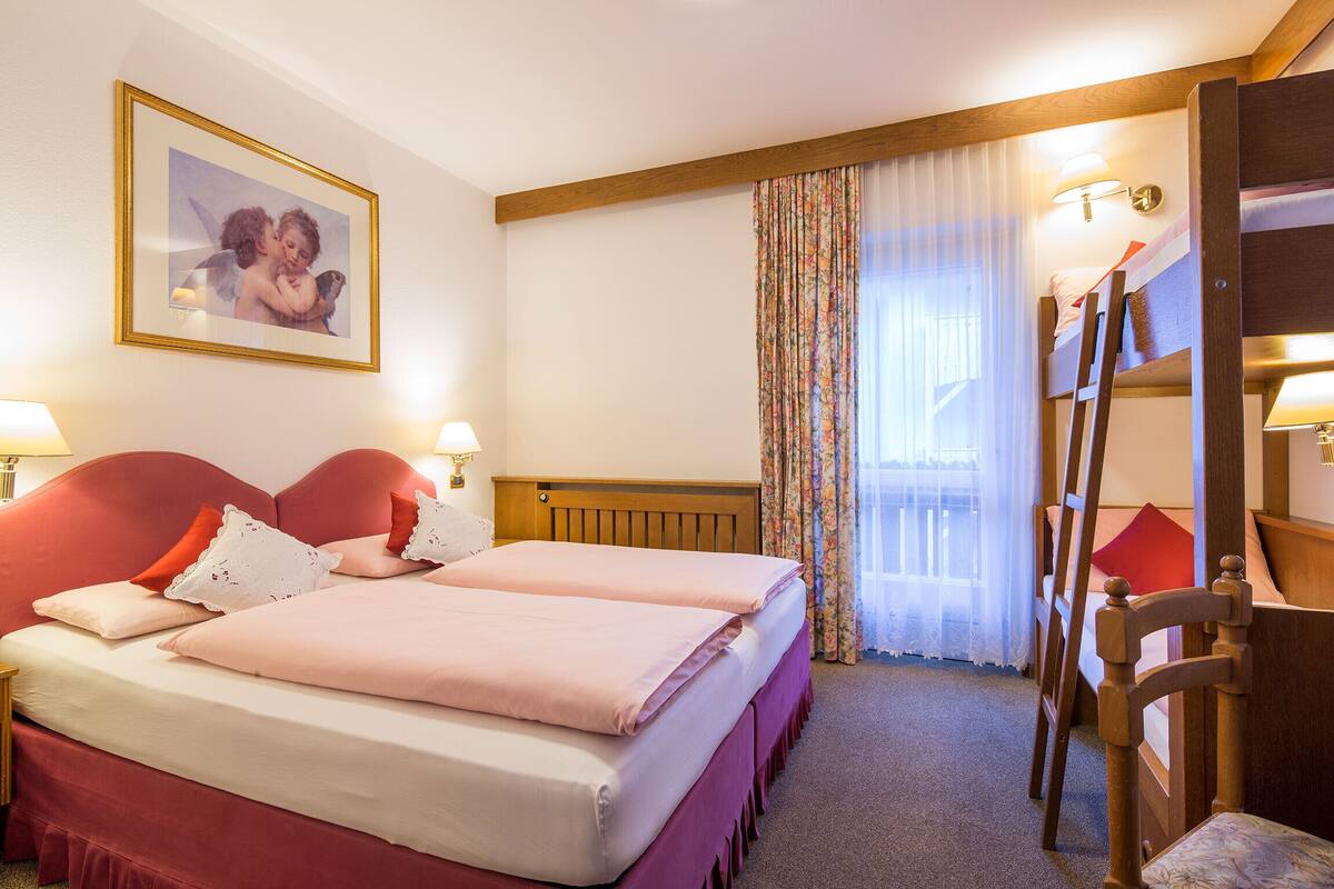 A hotel room with two beds, a wooden headboard, a ladder, a window with sheer curtains, and a framed picture on the wall.