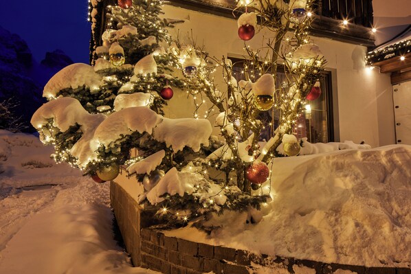 A snow-covered Christmas tree with ornaments and lights in front of a building. - Maria Hotel (Corvara in Badia)