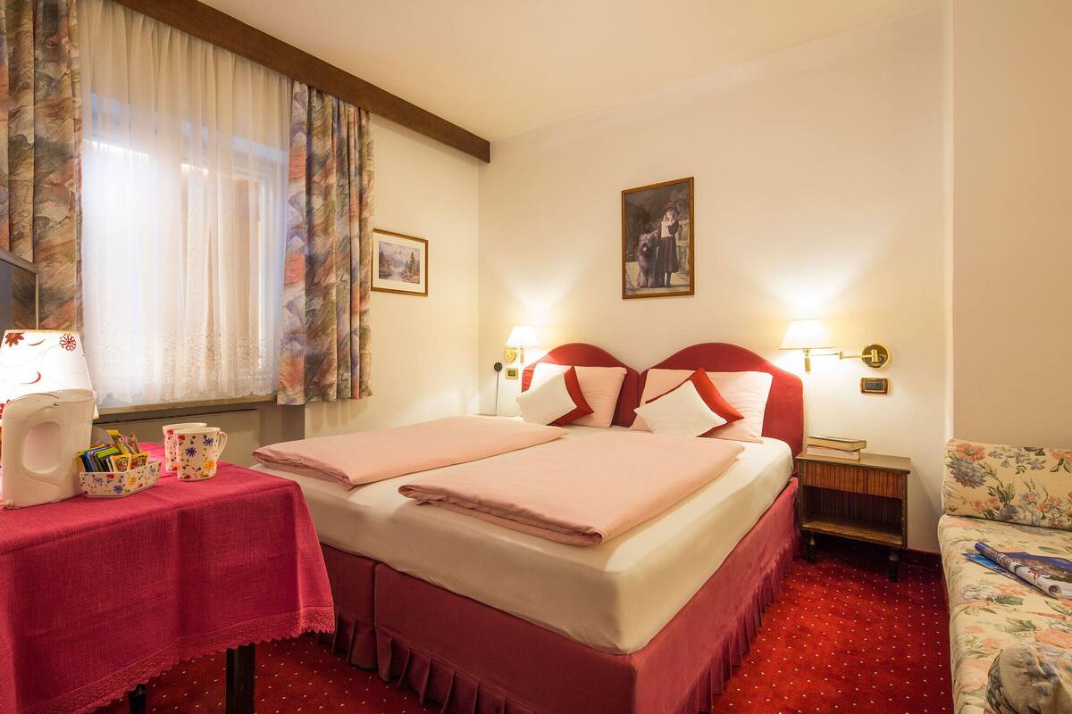 A hotel room with a bed, a desk with a lamp, a chair, and a window with curtains.