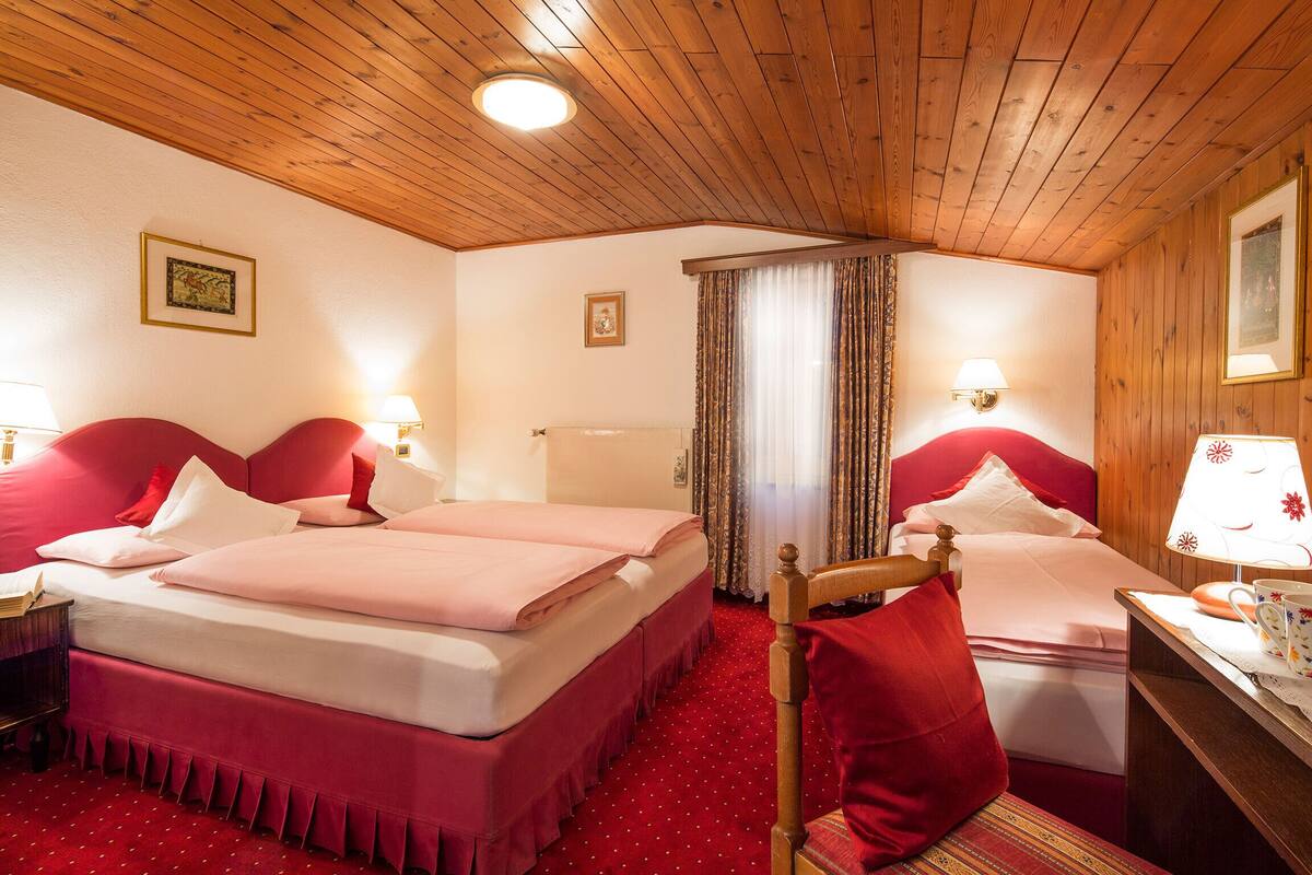 A hotel room with two beds, wooden ceiling, red carpet, and two bedside lamps.
