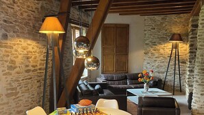 Um quarto aconchegante com teto de madeira, paredes de pedra, um tabuleiro de xadrez sobre uma mesa branca e cadeiras modernas.