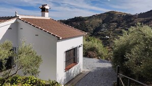 A white building with a tiled roof, a chimney, and a gravel driveway leading to a gate.