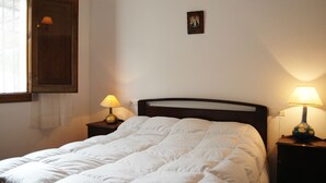 A neatly made bed with a white duvet, two bedside lamps, a small framed picture on the wall, and a window with curtains.
