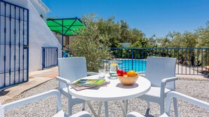 A patio with a table set for two, a bowl of fruit, and a magazine.