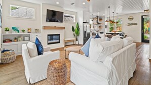 A modern living room with white sofas, a fireplace, a TV, and a ceiling fan. - The Pinetree Retreat | Near Beach, Pet Friendly Lux Home (Panama City Beach)