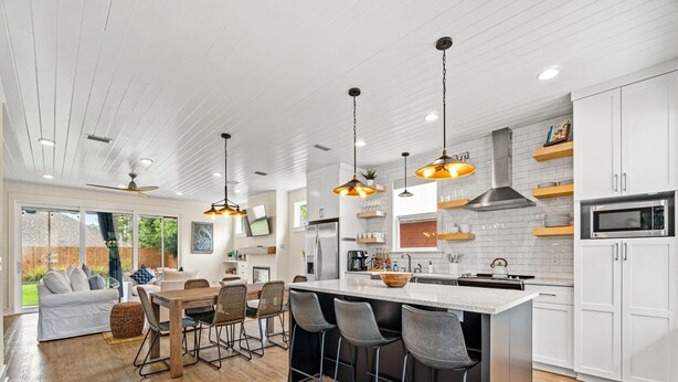 A modern kitchen with a large island, bar stools, and a dining area with a sofa and chairs. - The Pinetree Retreat | Near Beach, Pet Friendly Lux Home (Panama City Beach)