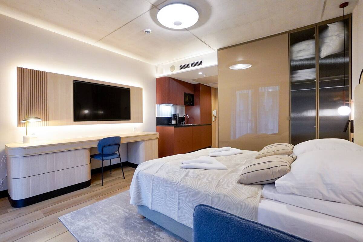 Una habitación de hotel moderna con cama, escritorio, silla, kitchenette y baño.