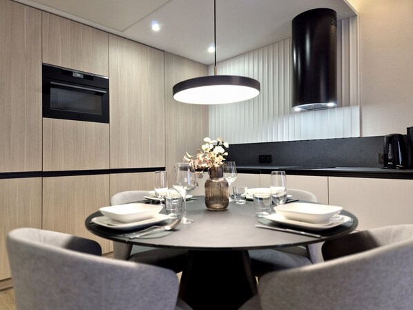A modern dining area with a round table set for six, equipped with plates, glasses, and cutlery. - Loft Premium Apartments by Baltic Home (Swinoujscie)