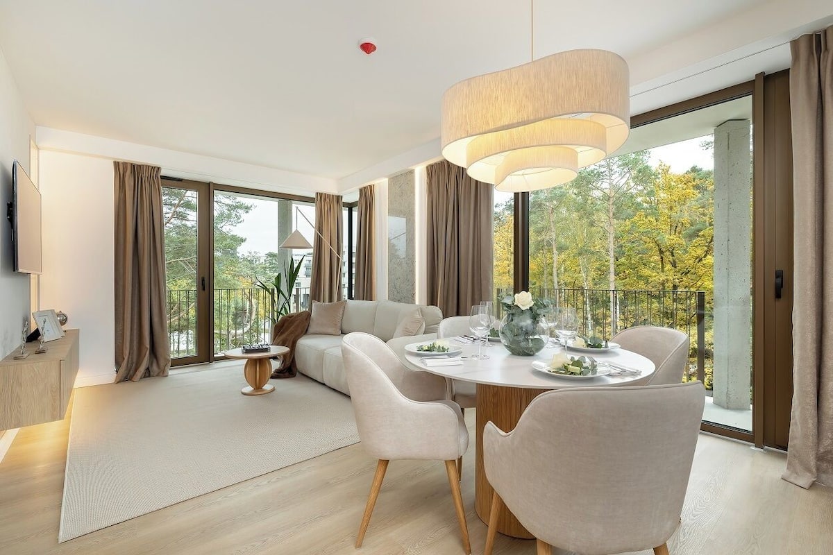 Una sala de estar moderna con comedor, ventanas amplias y vista a árboles.