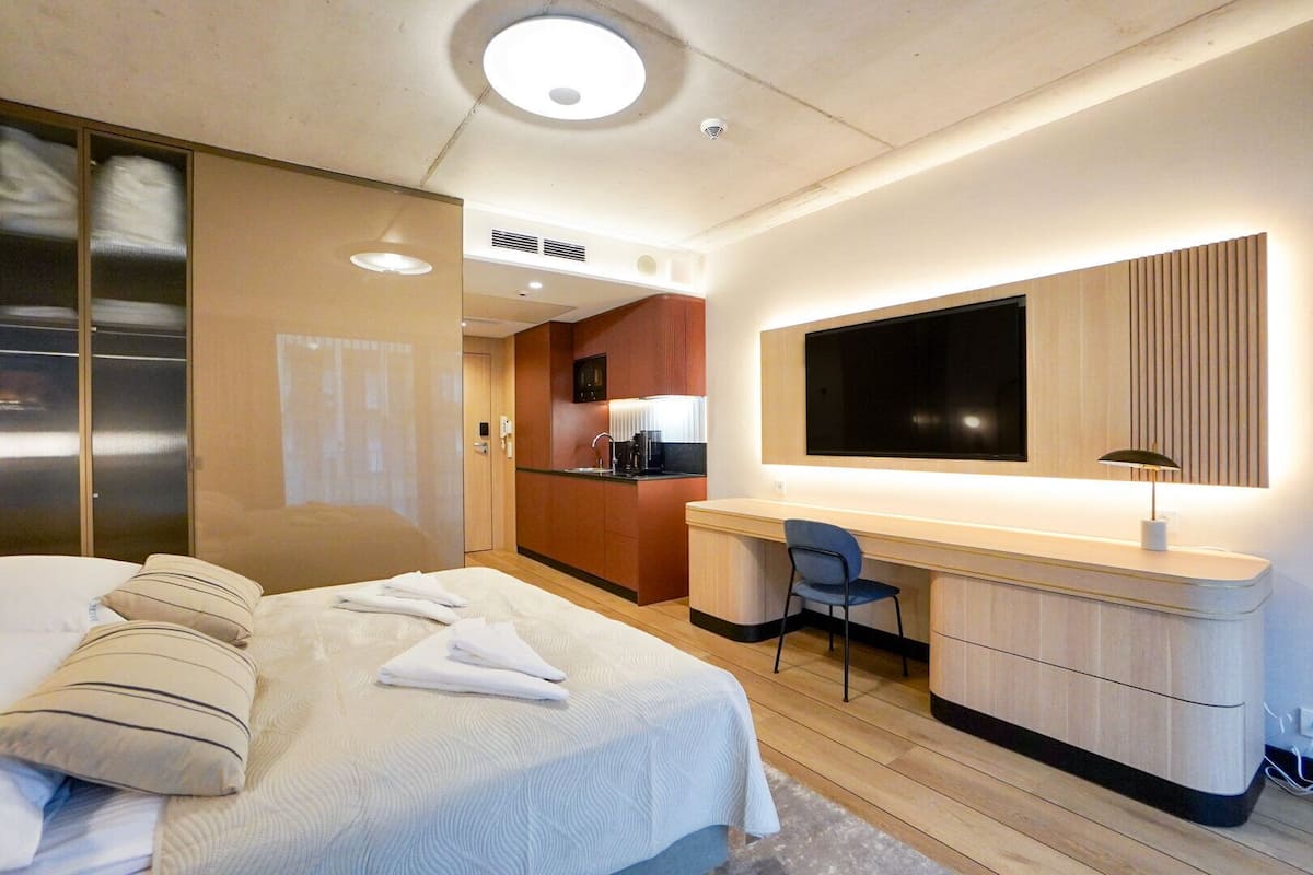 Habitación de hotel con cama, escritorio, silla, televisión y kitchenette.