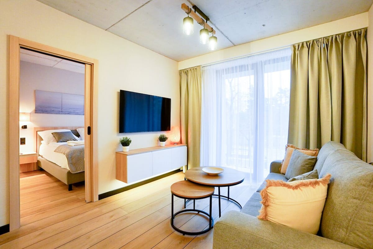 Una habitación de hotel moderna con cama, sofá, una mesita, televisión y ventana con cortinas.