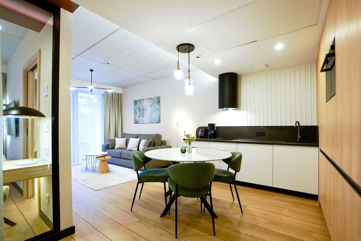 Una cocina moderna con una mesa de comedor redonda y sillas verdes, un sofá gris y una lámpara colgante negra.