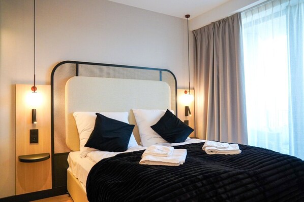 A neatly made bed with black and white bedding, two bedside lamps, and a window with curtains. - Loft Premium Apartments by Baltic Home (Swinoujscie)
