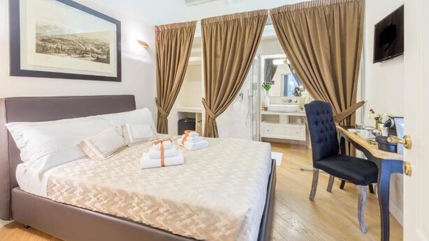Un lit bien fait, recouvert d’une couvre-lit à motifs, une table de chevet avec une lampe, une chaise et un bureau avec un ordinateur.
