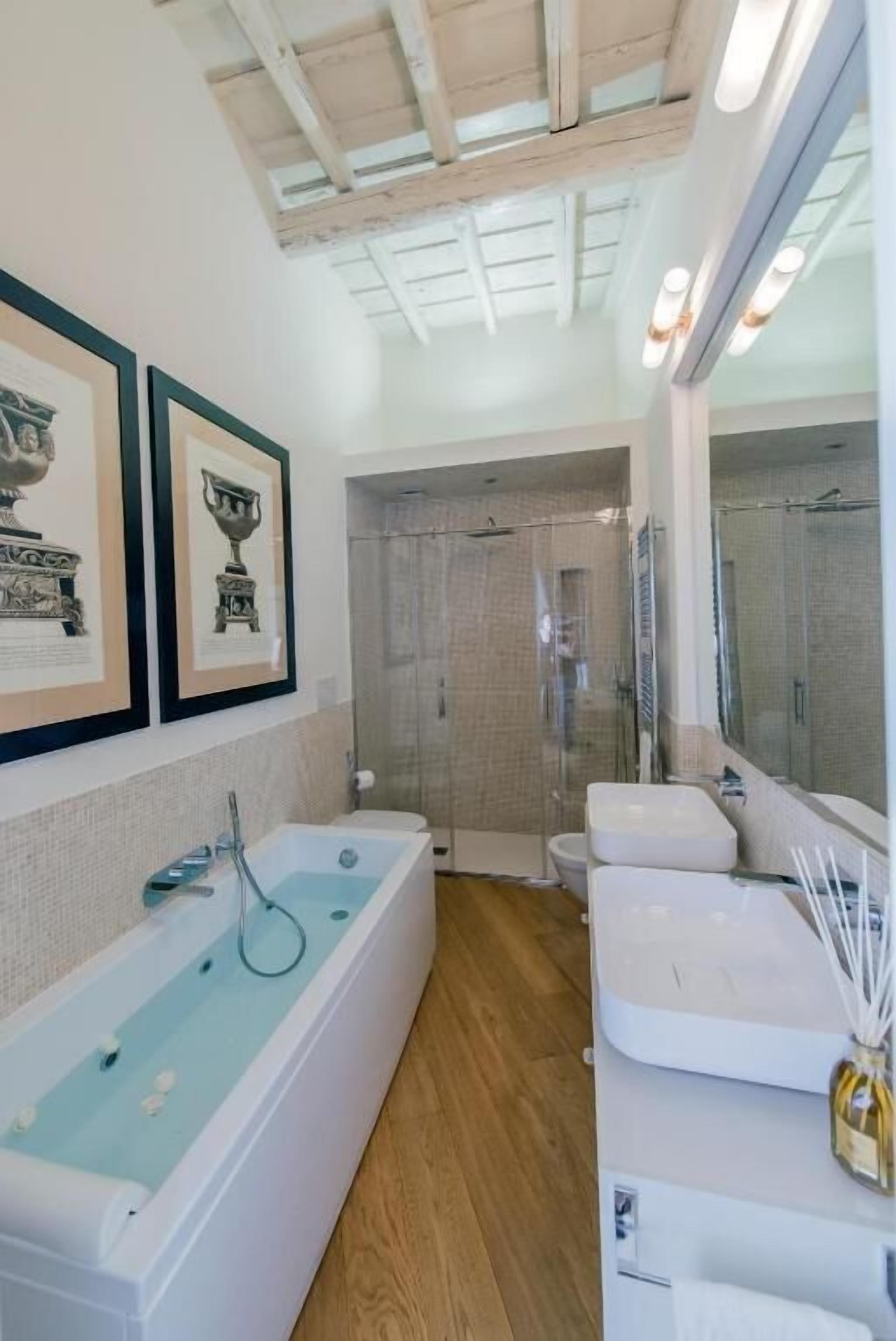 A modern bathroom with a bathtub, two sinks, a shower, and framed artwork on the wall.