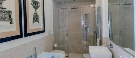 A modern bathroom with a bathtub, two sinks, a shower, and framed artwork on the wall.