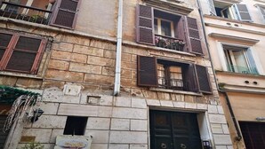 Un bâtiment à la façade en pierre, doté de nombreuses fenêtres avec volets et d’une porte noire.