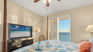 Ein Hotelzimmer mit Bett, Fernseher, Balkon und Meerblick sowie Deckenventilator.
