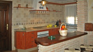 A kitchen with a wooden countertop, a sink, and a stove. There is a basket of fruit on the counter and a window with curtains.