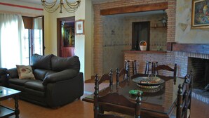 A living room with a leather sofa, a glass-top dining table, and a brick fireplace.