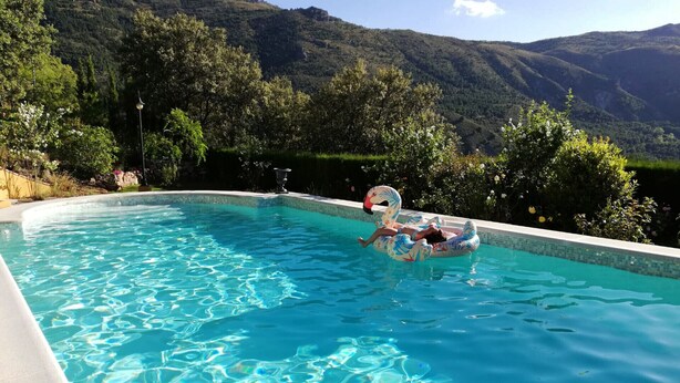 A swimming pool with clear blue water, surrounded by lush greenery and mountains in the background.