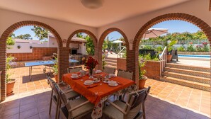 Eine Terrasse im Freien mit Esstisch, umgeben von Backsteinbögen, einem Pool und einem Garten.