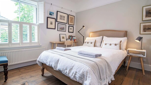 A bedroom with a wooden bed, white bedding, a desk, and a chair.