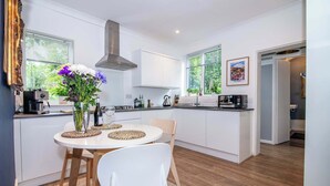 A modern kitchen with white cabinets, a central island with a round table, and a large window.
