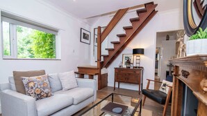 A living room with a light grey sofa, a glass coffee table, a wooden staircase, and a fireplace.