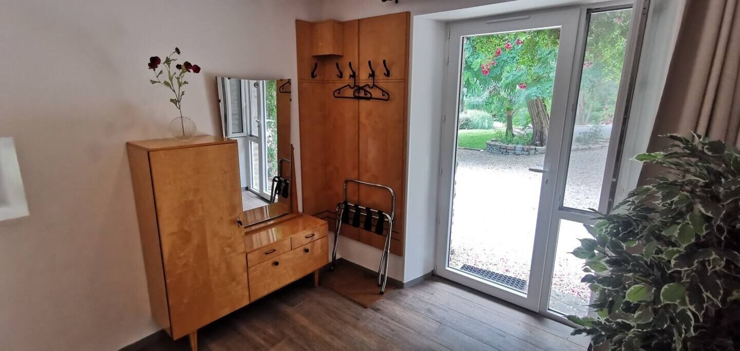 A room with a wooden wardrobe, a mirror, a coat rack, and a potted plant.