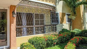 A two-story building with a balcony, a number '2' sign, and a garden with red flowers. - Residential Paradise V Apartments (Santo Domingo Norte)
