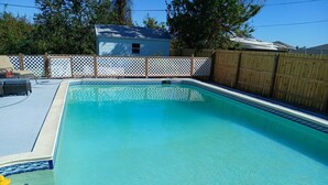 Una piscina rectangular con agua azul cristalina, rodeada por una valla de madera y un panel de celosía blanca.