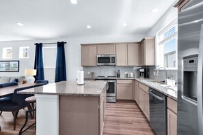 A modern kitchen with a central island, stainless steel appliances, and light wood cabinetry.