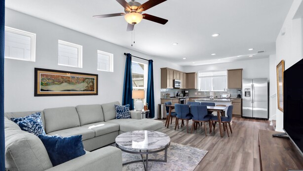 Un salon moderne avec un canapé, une table basse et un ventilateur de plafond. Il y a également un coin cuisine avec une table à manger et des chaises.