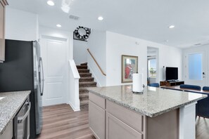 Una cocina moderna con refrigerador integrado, encimeras de granito y una escalera de madera que conduce a una sala de estar con televisor y asientos.