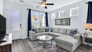 Un salon moderne avec un canapé d’angle, une table basse ronde et un ventilateur de plafond.