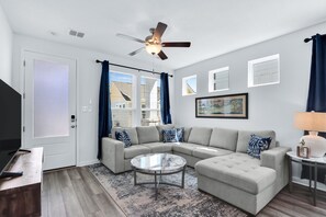 A modern living room with a sectional sofa, a round coffee table, and a ceiling fan. - Gorgeous 2 BDR Cottage Minutes to Everything NBTX! (New Braunfels)