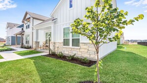 Une maison moderne à deux étages, avec des fondations en pierre, une pelouse bien entretenue et un arbre dans le jardin.