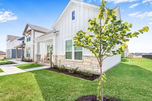 A modern two-story house with a stone foundation, a well-maintained lawn, and a tree in the front yard. - Gorgeous 2 BDR Cottage Minutes to Everything NBTX! (New Braunfels)