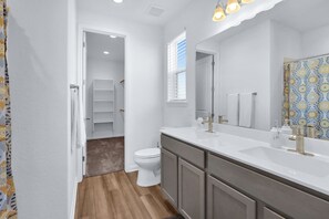 A modern bathroom with a white vanity, a large mirror, and a shower area. - Gorgeous 2 BDR Cottage Minutes to Everything NBTX! (New Braunfels)