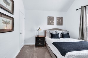 Une chambre à coucher avec un lit, une table de chevet, une lampe et une œuvre d’art accrochée au mur.
