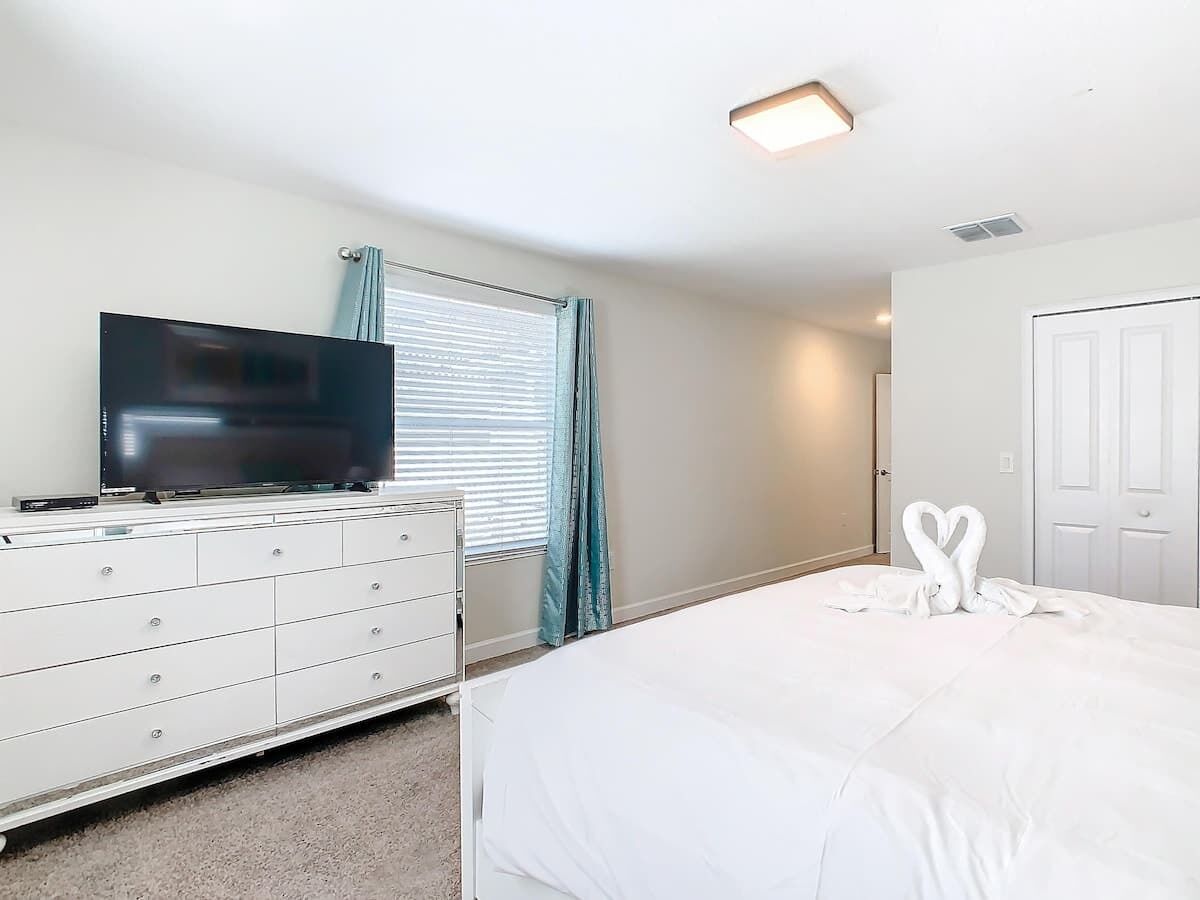 A bedroom with a bed, a dresser, a television, and a door.